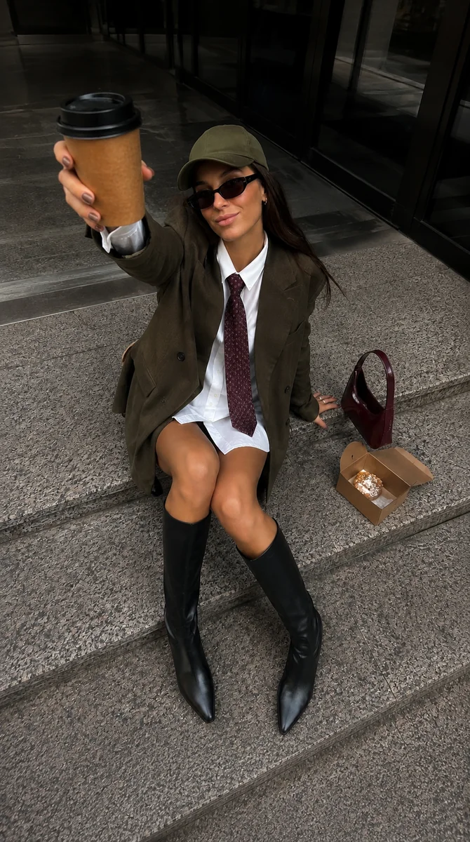 Original photo: an adult woman sitting on city steps in an olive blazer, white shirt, and black boots, holding a coffee cup